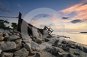 Silhouette image of abandon shipwrecked on rocky shoreline. dark cloud and soft on water