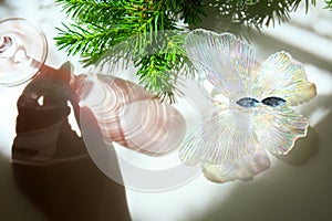 Blurred shadow of female hand and wine glass with light passes through glass.  branch of Christmas tree and christmas butterfly