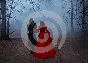 Blurred silhouette of a Gothic couple. Two people walks in the blue fog. A vampire man in a black tailcoat with long