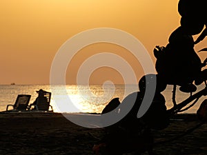 Blurred silhouette of a woman with a hat sitting enjoying the sunset on the ocean with a ship on the horizont and leaves of a tree