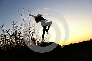 Blurred silhouette of young slender girl posing over beautiful sunset background.