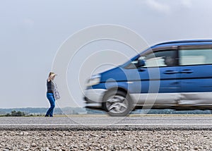 Blurred silhouettes of a fast-moving car and a woman standing on the side of the road