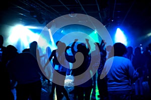 Blurred silhouettes of a group of people dancing in a nightclub on the dance floor under colorful spotlights