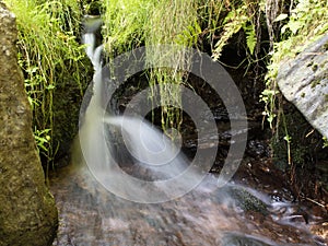 Blurred stream of a mountain stream bounces off a stone photo