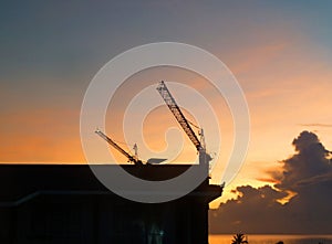 Blurred Sunrise and cloudy sky over ocean and silhouette of big tower crane lifting up construction materials.