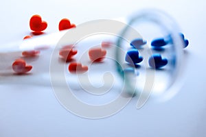 A blurred test tube in the foreground closes the letters IVF from red and blue hearts. Concept of in vitro fertilization