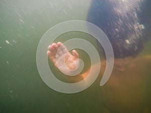 Blurred underwater shot of sinking or drowning person in green turbid water