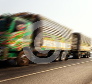 Blurred, unrecognizable trucks carry goods along highway