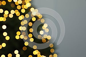 Blurred view of beautiful fir tree with Christmas lights on grey background, closeup. Space for text