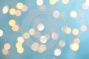 Blurred view of festive lights on light blue background. Bokeh effect