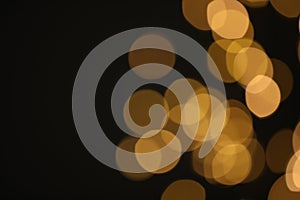Blurred view of golden lights on black background, space for text. Bokeh effect