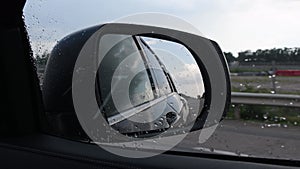 Blurred view in side mirror of fast moving car in rainy weather