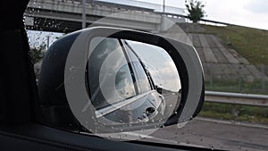 Blurred view in side mirror of fast moving car in rainy weather