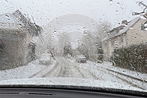 Blurred view of snow covered street through wet windshield of car on snowy, rainy spring day