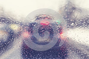 Blurred view through the windshield of a car with raindrops on the stop signals car. Concept of drive safety on the road