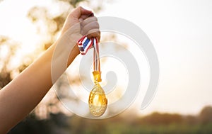Blurred of woman hands raised and holding gold medals with Thai ribbon against blue sky background to show success in sport or