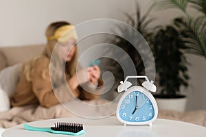 Blurred woman with phone, hairbrush and alarm clock in focus
