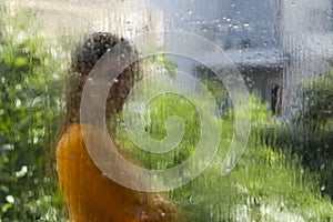 Blurred woman silhouette through wet window glass