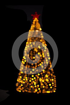 Blurred yellow Christmas tree lights on black isolated background. Design element. Defocused spruce with star