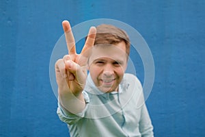 Blurred young man in blue shirt posing in blue background with hand showing the victory sign
