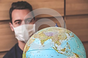 Blurred young man traveller in medical face mask looking at world globe. Coronavirus quarantine. Travel restrictions caused by the