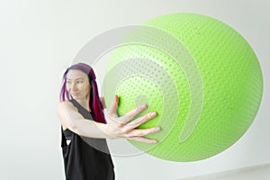 Blurred young positive cheerful girl hipster holding a green fitball in her arms during classes in the gym. Concept of