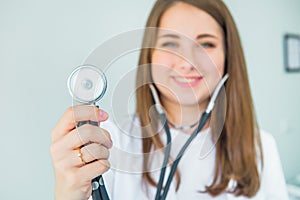 Blurred Young smiling female doctor holding her stethoscope to insinuate that it`s time for a check up in clinic on white backgro