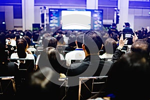 Blurry of auditorium for shareholders` meeting or seminar event with projector and white screen, many business people listening o photo