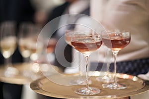 Blurry background of the waiter holds the tray with a glass of champagne to be served