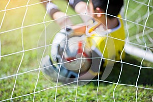 Blurry of ball in hand of goalkeeper on green grass at goal. Goalkeeper is catching the soccer ball. Asian boy soccer player