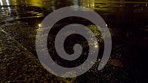 Blurry cars passing by in the rain at night, with reflections in a puddle