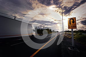 Blurry container truck drive through U-turn sign during sunset  on country road