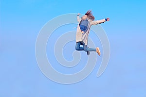 Blurry image of a happy teenage girl jumping up, blue sky background, horizontal view. People, freedom, travel concept.