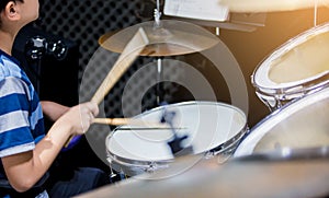Blurry image of wooden drumsticks in hands of Asian kid wearing blue striped t-shirts to learning and play drum set in music room