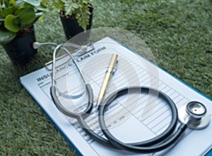 The blurry light design background of the stethoscope and insurance claim form put on green grass ground floor