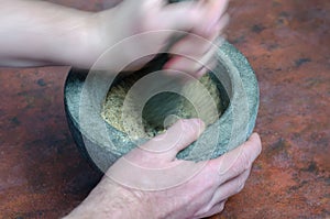 Blurry motion. A hand grinds with a pestle spices and herbs in a gray stone mortar
