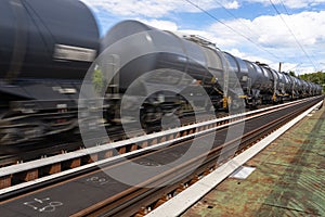 Blurry photo of railroad tank cars in motion, on a metal bridge over the river.