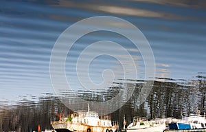 Blurry reflection of boats, trees, sky and clouds in river