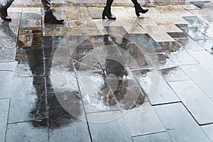 Blurry reflection legs and shadows, silhouettes of the people in the wet sidewalk, in a puddle of people walking on a