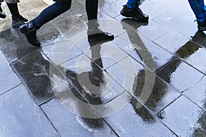 Blurry reflection legs and shadows, silhouettes of the people in the wet sidewalk, in a puddle of people walking on a