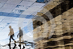 Blurry reflection shadow silhouettes of  two young men walking on a vintage pavement on wet city street