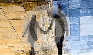 Blurry reflection shadow silhouettes of  a young couple walking on a rainy summer day