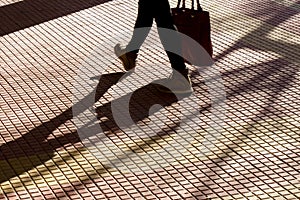 Blurry silhouette shadow of legs of a person carrying a bag while walking on tiled street sidewalk photo