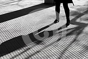 Blurry silhouette shadow of legs of a woman in high heels walking alone on tiled pedestrian walkway