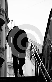 Blurry silhouette of a young man walking alone up the city subway stairs with hands in pockets