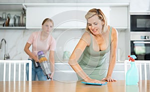 Blurry teen girl help mother doing housework in kitchen, mom cleaning dining table