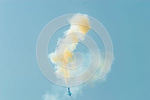 Blurry view of an aerobatic plane leaving a white and yellow smoke trail in the blue sky.