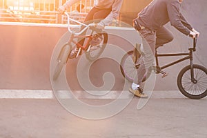 Bmx riders make tricks in a skate park on the background of the sunset. Evening training BMX cyclists. Bmx Concept