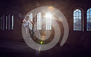 BMX stunt and jump riding in a hall with sunlight.