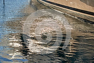 Board of the big boat of gold color, golden reflections of the sun on water at sunset, interesting texture, smooth lines